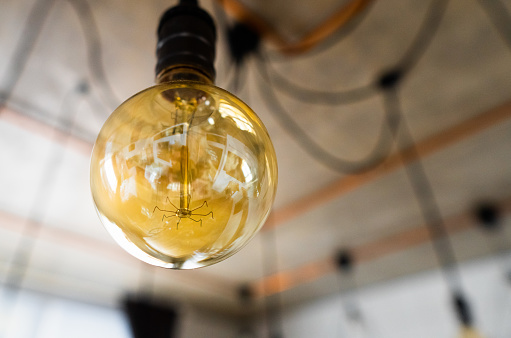 Close-up of big incandescent light bulb hanging in modern kitchen. Decorative antique edison light bulb with straight wire. Inefficient filament light bulb waste electricity. E27, dimmable, warm white