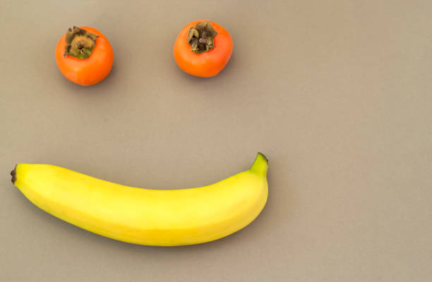 istock Smiling face made from fruit persimmon and banana beige background. 1220806590