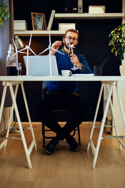 istock Young innovative dedicated bearded employee sitting in his modern office and drawing sketches of windmills. Sustainable development concept. 1220807775
