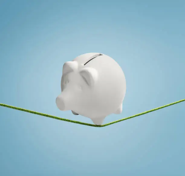Piggy bank balancing precariously on a thin line ready to fall down