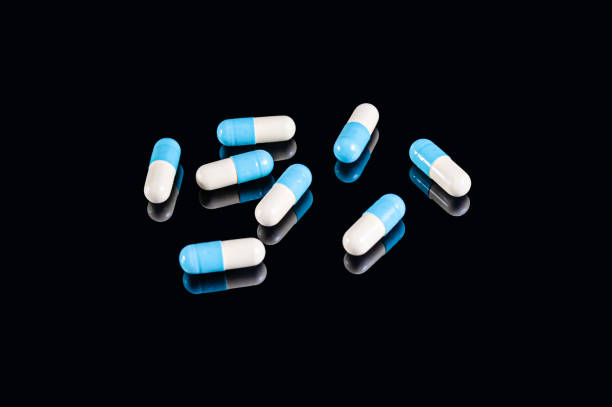 istock Blue and white two-piece capsules on an isolated black background with reflection 1220813514