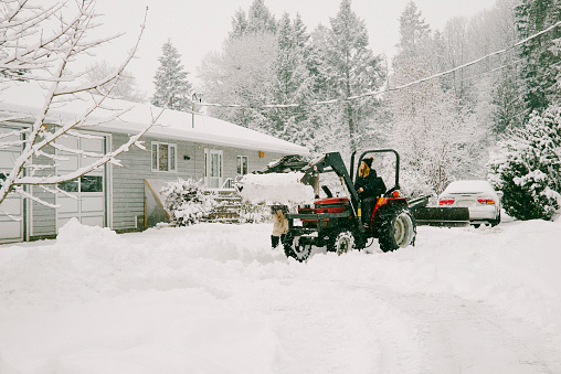A young woman using a tractor to clear the snow from in front of a home in British Columbia, Canada.