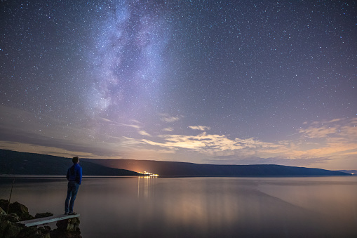 Rear view of a adult man standing on a seashore under a Milky Way in the sky at night