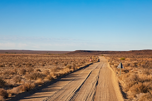 Corrugated gravel road with dip and curve in drought-stricken Karoo region of Northern Cape, South Africa