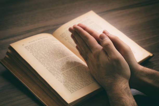 istock Hands clasped in prayer over a Holy Bible, wooden table background. 1220820897