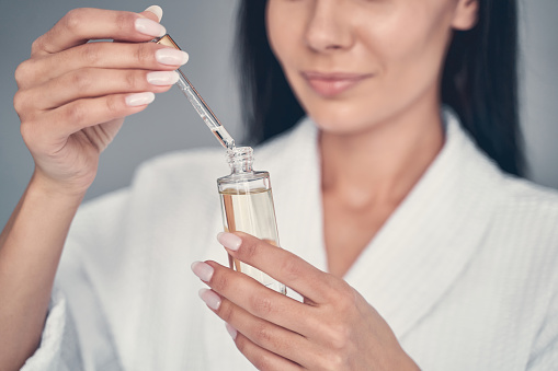 Cropped photo of a Caucasian female in a waffle weave bathrobe examining a face serum