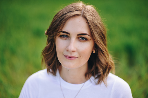 The girl is blonde, brown hair, in a white shirt and blue midi skirt. Walking in the field, through the green grass. Portrait of a girl. Positive and smile.