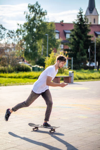 istock Young man skateboarding on street and using smart phone 1220821991