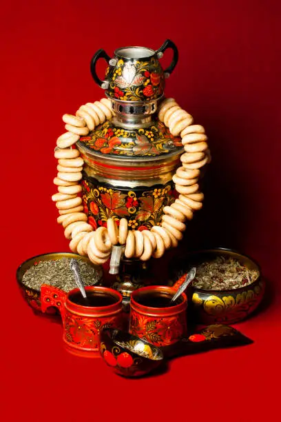 Samovar and drying with black tea in wooden mugs on a red background. Russian folk traditions.