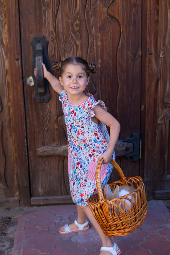 funny five year old girl comes into a wooden house holding a basket with a rabbit in her hands