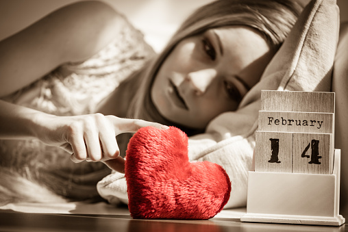 Sad or serious woman feeling lonely and unloved druing Valentines Day holding little red pillow in heart shape.