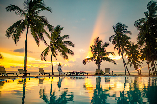 Young blonde woman walking by swimming pool at tropical beach with palm trees at scenic sunset, Zanzibar, Tanzania