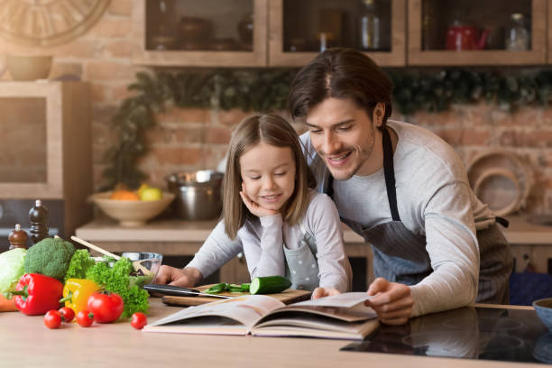 istock Smiling Little Girl And Her Dad Checking Ingredients In Coolinary Book 1220827340