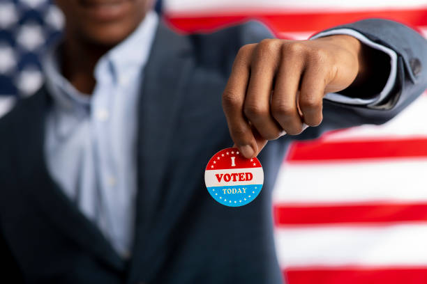Unrecognizable african citizen of America holds I voted today Unrecognizable african citizen of America holds I voted today button, typical of US elections on American flag. midterm election photos stock pictures, royalty-free photos & images