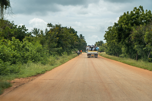 Rear view shot of a large group of people riding on the back of a truck along a road,  Zanzibar,  Tanzania