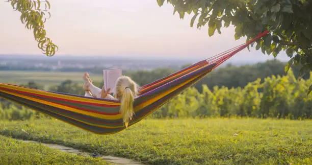 Photo of Woman reading a book in hammock in the nature at sunset