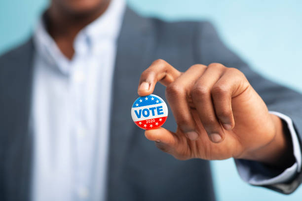 afrikanischer mann hält abstimmungsknopf auf blauem hintergrund - voting usa button government stock-fotos und bilder