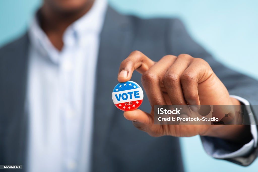 Hombre africano sosteniendo botón de voto sobre fondo azul - Foto de stock de Votar libre de derechos