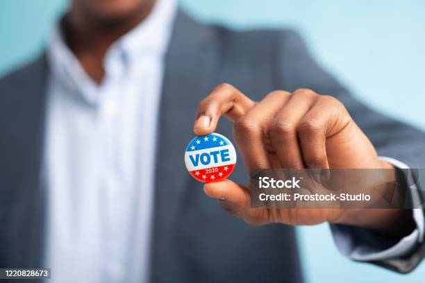 Hombre Africano Sosteniendo Botón De Voto Sobre Fondo Azul Foto de stock y más banco de imágenes de Votar