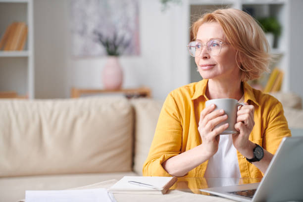 istock Serene mature female with short blond hair having coffee while working remotely 1220830304