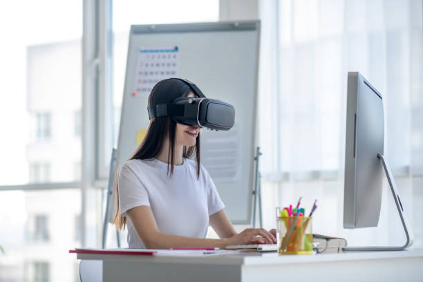 istock Dark-haired girl working at the computer wearing vr headset 1220834701