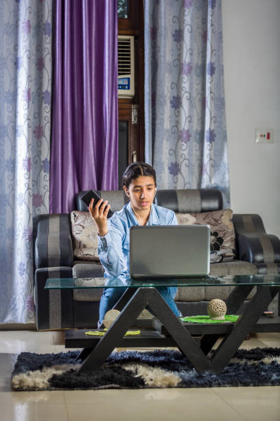 une fille utilisant l’ordinateur portable et le téléphone mobile simultanément - indian girls audio photos et images de collection