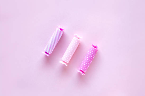 Three candy in polka dot wrapper on pink background. Lip balm sticks.