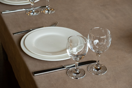 The served table in the restaurant. Clean dishes and appliances on the tablecloth in a cafe. Shiny transparent glasses. White plates. Prepared for the reception of guests. High service.