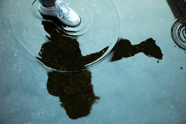 Woman walking in the city rain. Reflection of female silhouette in urban city puddle. water waves moving inside puddle from white sport shoe. Abstract concept shot.