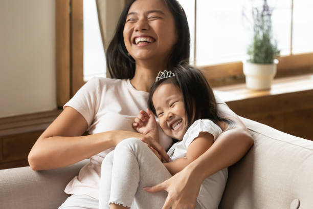 overjoyed asian mother tickling little daughter having fun at home - tickling imagens e fotografias de stock