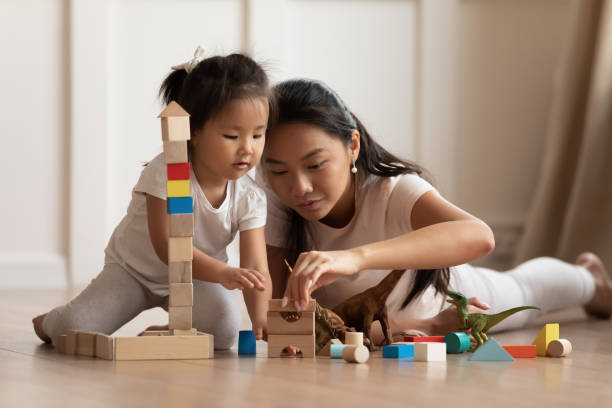 Daughter her vietnamese mother play on warm floor with blocks Involved little daughter her vietnamese mother play on warm floor using wooden colorful blocks create towers and buildings improve fine motor skill of kid. Funny educational games for children concept asian nanny stock pictures, royalty-free photos & images
