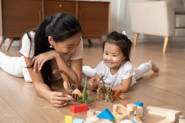 Lying on warm floor asian mother play with little daughter Lying on warm wooden floor asian mom play game with little daughter holds dinosaurs toys heap of colorful construction blocks nearby. Spend time have fun together educational activity with kid concept hot vietnamese women pictures stock pictures, royalty-free photos & images