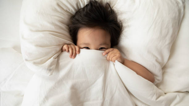 istock Vietnamese girl lying in bed hides her face under blanket 1220837303