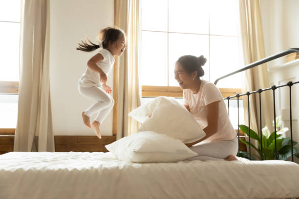 beztroska mała córka skacze na łóżku, podczas gdy wietnamska matka śmieje się - action family mother sport zdjęcia i obrazy z banku zdjęć