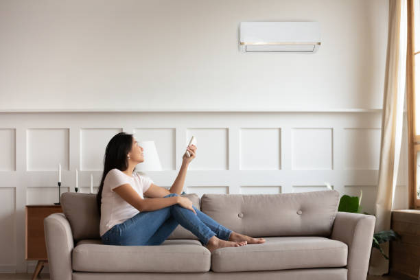 istock Vietnamese woman switching on air conditioner while resting seated indoors 1220837356