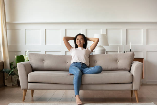 Asian woman resting on couch enjoy fresh air at home Asian woman looks at distance resting leaned on couch enjoy fresh air in summer day in modern fashionable living room interior, full length image. Contemporary apartments owner or carefree day concept hot vietnamese women pictures stock pictures, royalty-free photos & images