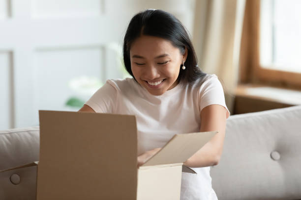 mulher vietnamita sentada no sofá abre pacote entregue se sente feliz - package box gift delivering - fotografias e filmes do acervo
