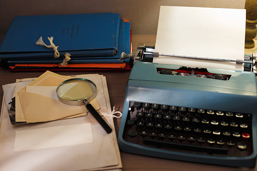 Investigator desk with confidential documents. Secret documents, vintage typewriter with blank paper, magnifying glass.