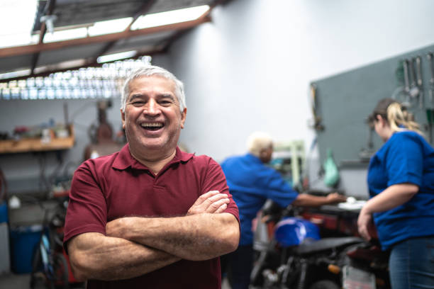retrato de hombre mayor sonriente con los brazos cruzados en reparación de automóviles - customer auto repair shop car mechanic fotografías e imágenes de stock