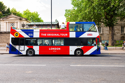 London, UK - June 21, 2018: Buckingham Palace and sign for Hop on Hop off The Original Tour double decker red white blue bus with people walking