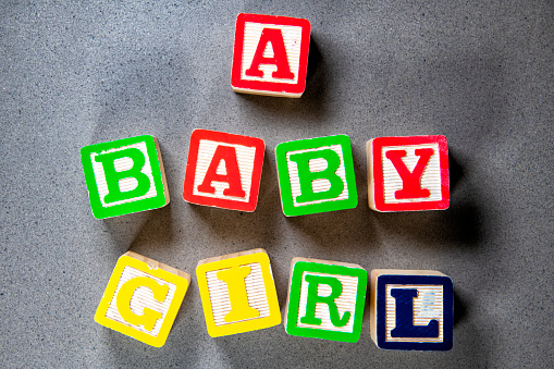 Baby block lettering spelled out to announce the birth of a baby girl shot in studio against a concrete background.