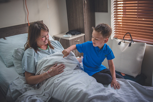 A mother and son share a moment in hospital for the arrival of the new baby brother. The boy is very excited sitting on the bed pointing at his mothers stomach.