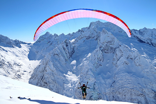 paraplane flying over snowy Caucasus mountains and sunny blue sky