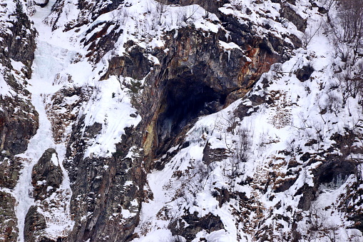 sheer cliff covered with snow and the entrance to the cave