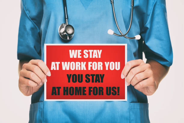 COVID-19 Coronavirus doctor holding sign for viral social media post showing: We Stay at Work for You, Please you stay at home for us! on card. Nurse with blue scrubs isolated on white background. covid-19 doctor coronavirus firma para la publicación de las redes sociales virales que muestra: nos quedamos en el trabajo para usted, por favor, quédese en casa para nosotros! en la tarjeta. enfermera con srubs azules aislados sobre fondo blanco