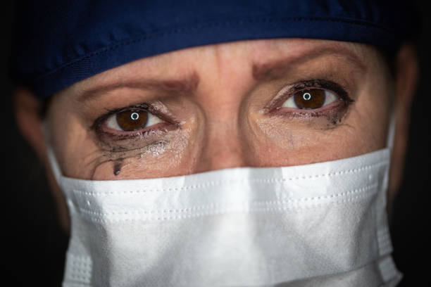 tearful stressed weibliche ärztin oder krankenschwester tragen medizinische gesichtsmaske auf dunklem hintergrund - overworked worried distraught front view stock-fotos und bilder