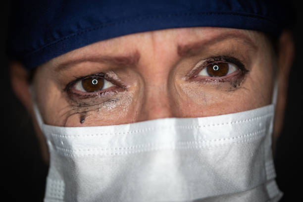 tearful stressed mujer doctora o enfermera que usa máscara facial médica en fondo oscuro - overworked worried distraught front view fotografías e imágenes de stock