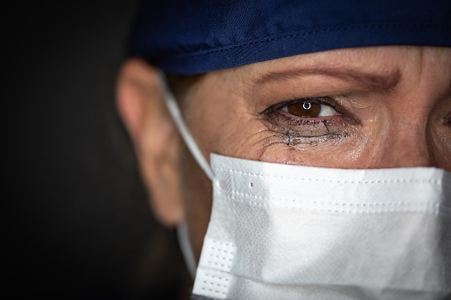 Tearful Stressed Mujer Doctora o Enfermera que usa máscara facial médica en fondo oscuro photo