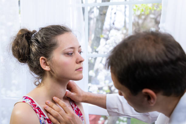 Doctor inspecting, doing palpation examination of young woman with Grave's disease hyperthyroidism symptoms of enlarged thyroid gland goiter and ophthalmopathy in hospital Doctor inspecting, doing palpation examination of young woman with Grave's disease hyperthyroidism symptoms of enlarged thyroid gland goiter and ophthalmopathy in hospital thyroid disease stock pictures, royalty-free photos & images