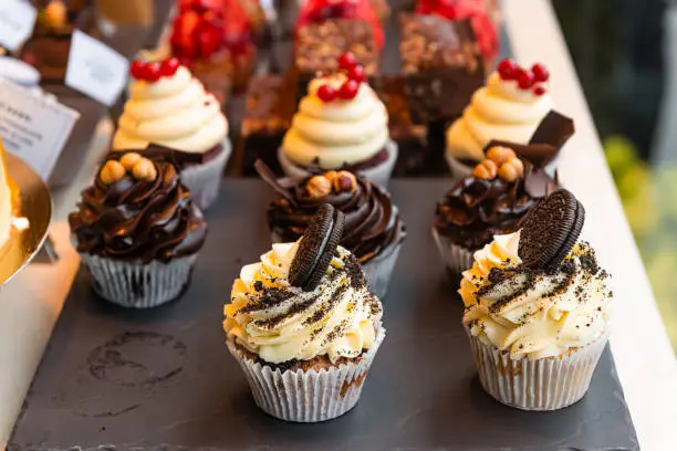 Photo of Chocolate and vanilla sandwich cookies cupcakes on display in gourmet bakery with muffin paper liners and frosting macro closeup